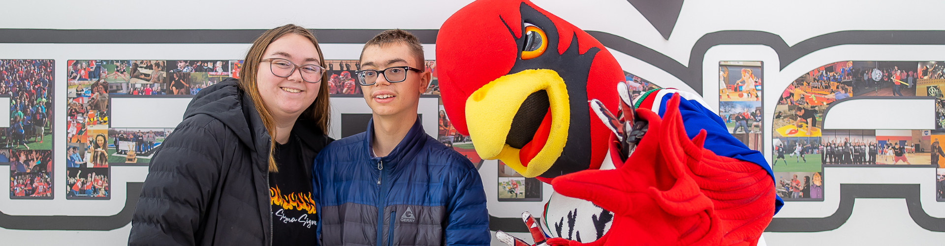 Two people posing next to Coop the Cardinal.